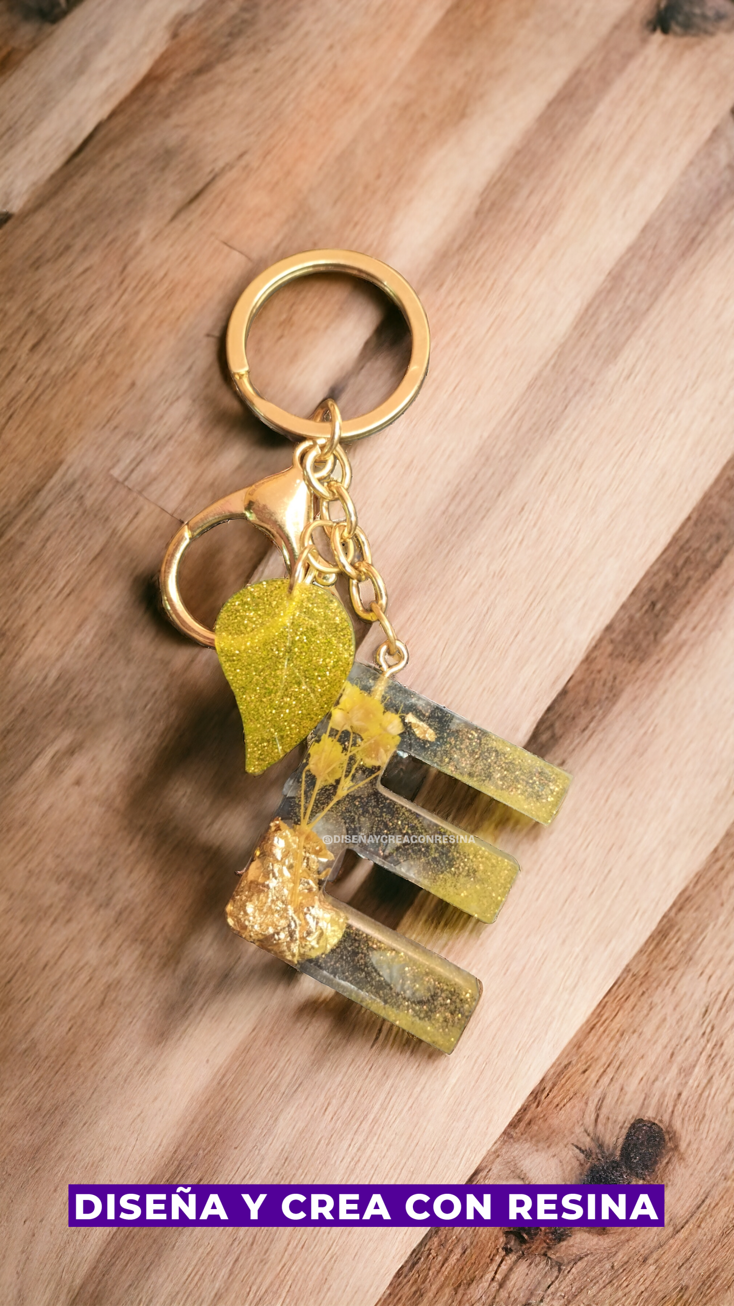 llavero color dorado con letra E mayúscula de color amarillo y transparente junto con ella también una hoja de árbol pequeña de color amarillo brillante