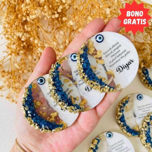 En la imagen se puede ver unos souvenirs circulares realizado con resina epóxica con colores blanco azul y dorado, con letras en negro