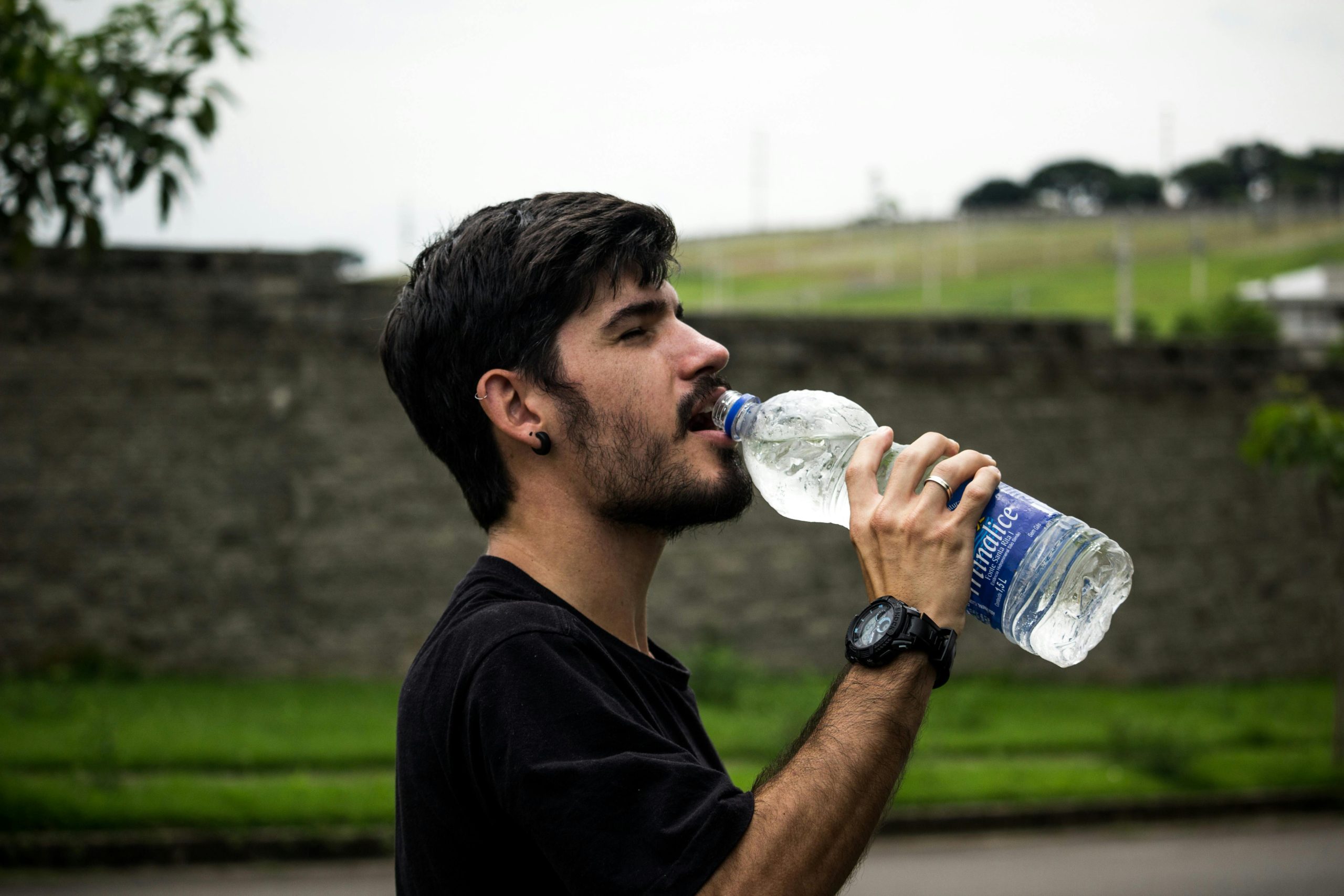 persona de sexo masculino bebiendo agua del pico de una botella de plástico