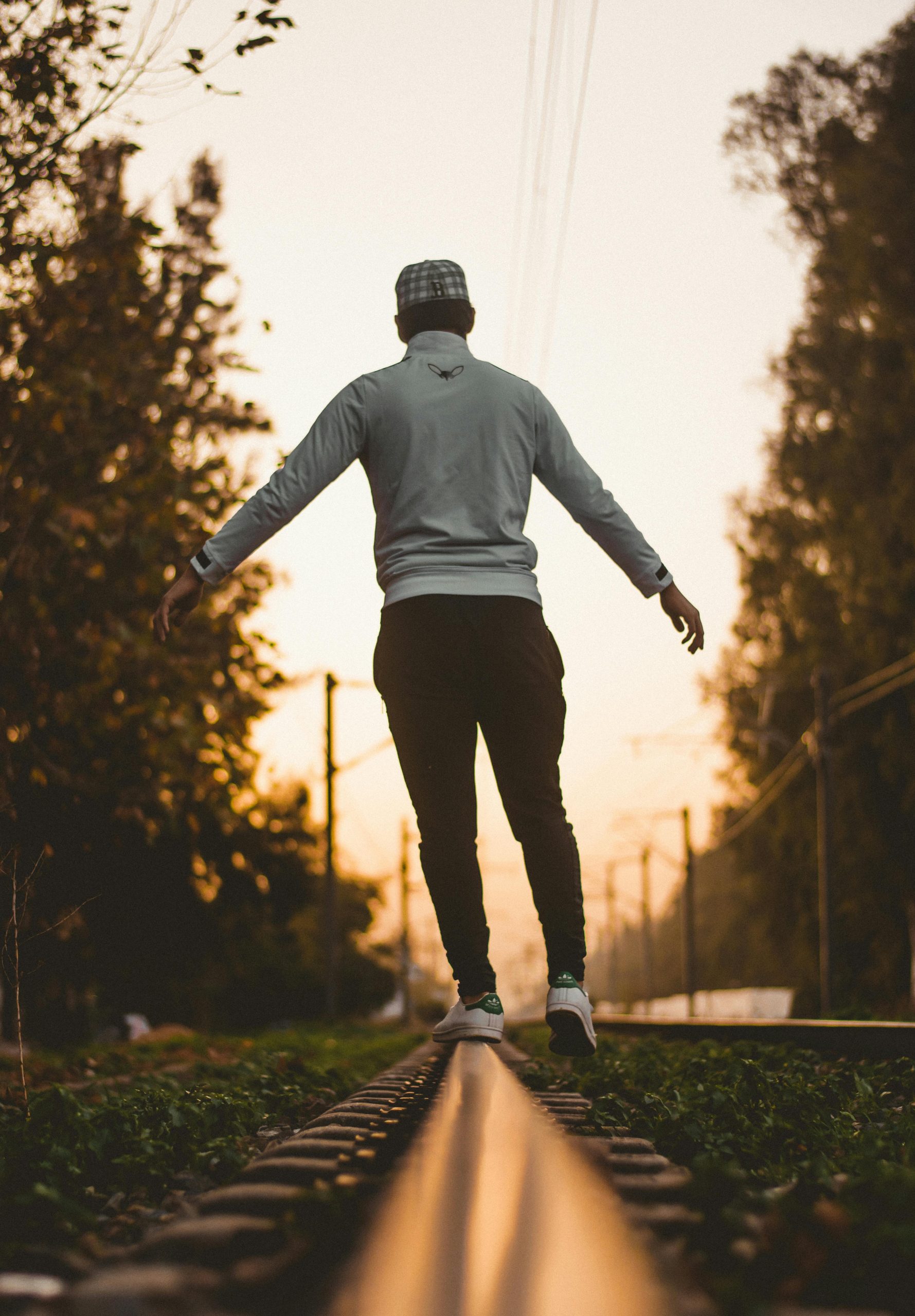 persona de sexo masculino de espaldas caminando sobre uno de los rieles de una vía de tren.